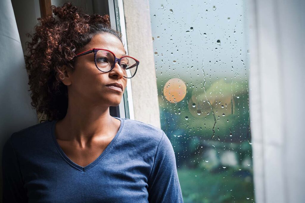 Woman wearing glasses looking out window and pondering, "What is buprenorphine?"