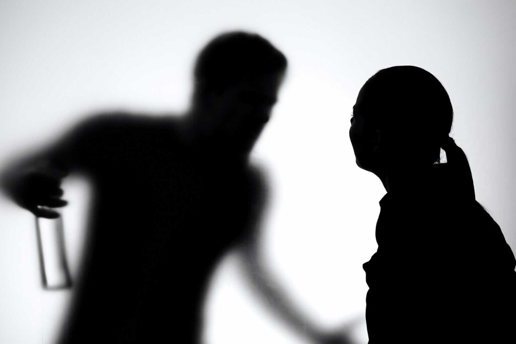 Silhouettes of a couple in a fight, both wondering, "Are alcohol and aggression linked?"