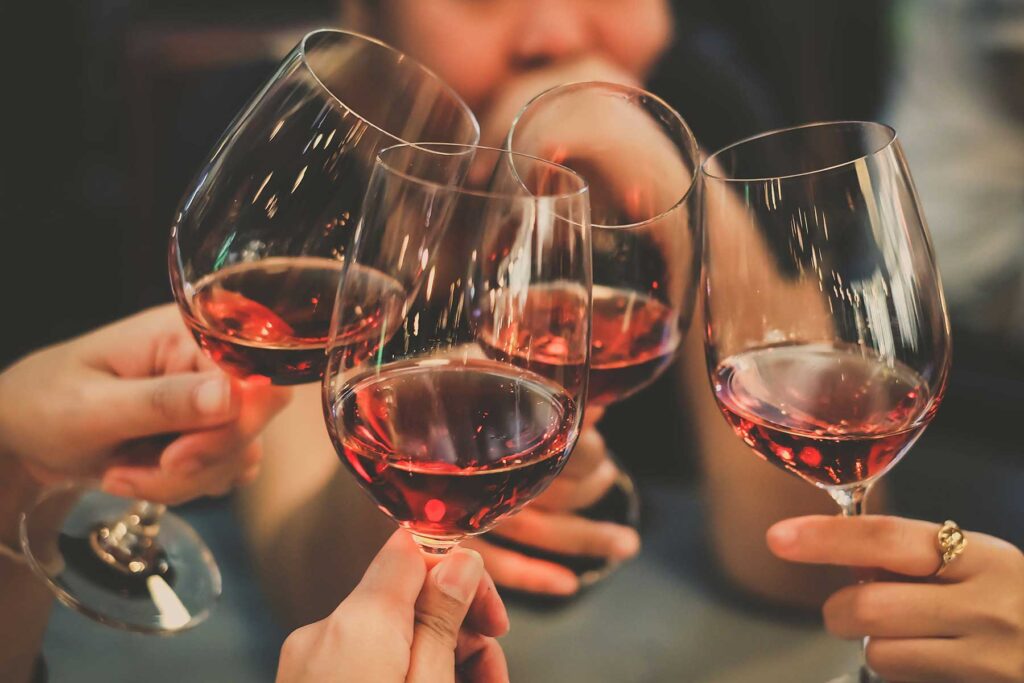 Hands of people clinking wine glasses, ignoring the dangers of wine culture